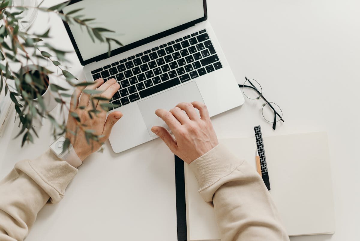 Close-up of hands typing on a laptop next to a cup of coffee on a wooden desk.